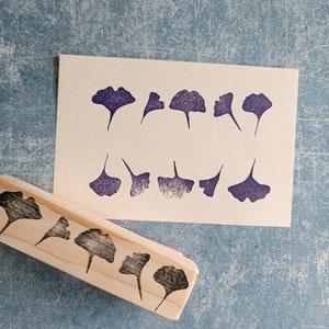 May include: A wooden stamp with a row of ginkgo leaf designs. The stamp is used to create impressions on paper.