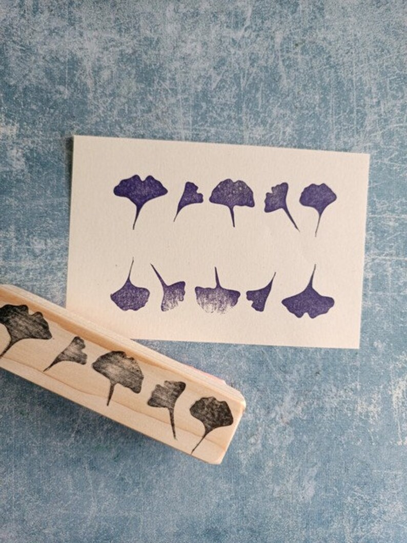 May include: A wooden stamp with a row of ginkgo leaf designs. The stamp is used to create impressions on paper.