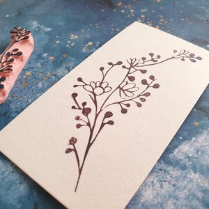 May include: A brown rubber stamp with a floral design. The stamp is on a light blue background with gold flecks.