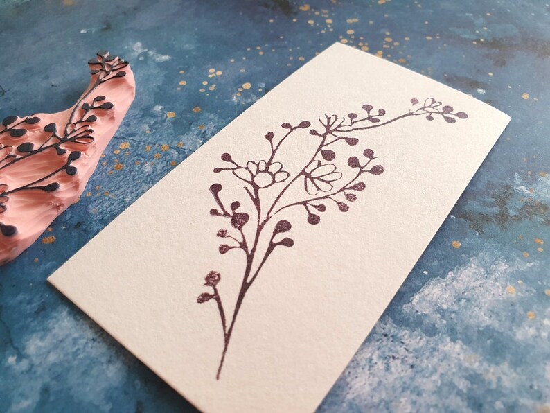 May include: A brown rubber stamp with a floral design. The stamp is on a light blue background with gold flecks.