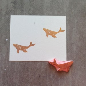 May include: A white card with two brown whale silhouettes printed on it. A pink whale rubber stamp is on the table below the card.