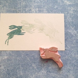 May include: A green rubber stamp of a rabbit jumping, with a pink rubber stamp of a rabbit jumping in the lower right corner.