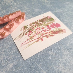 May include: Two pink rubber stamps with a floral design. The stamps are on a light blue textured surface. The stamps are used to create a floral print on paper.