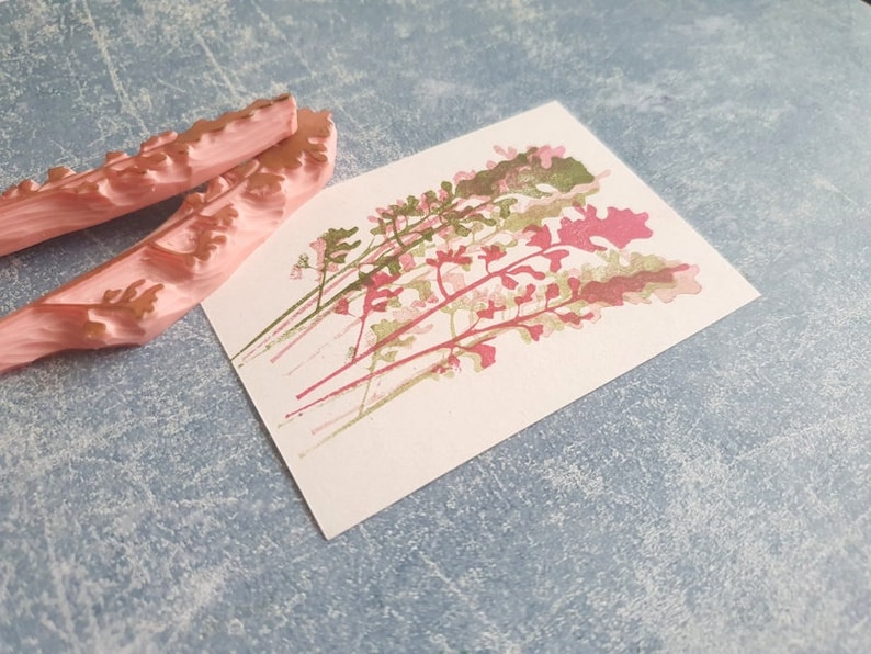 May include: Two pink rubber stamps with a floral design. The stamps are on a light blue textured surface. The stamps are used to create a floral print on paper.