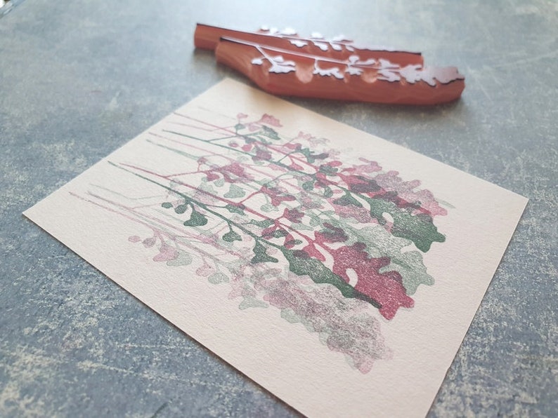 May include: A pink and green floral design stamp print on a cream coloured card.