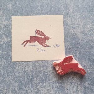 May include: A red rubber stamp of a running rabbit. The stamp is 2.7 inches by 1.8 inches.