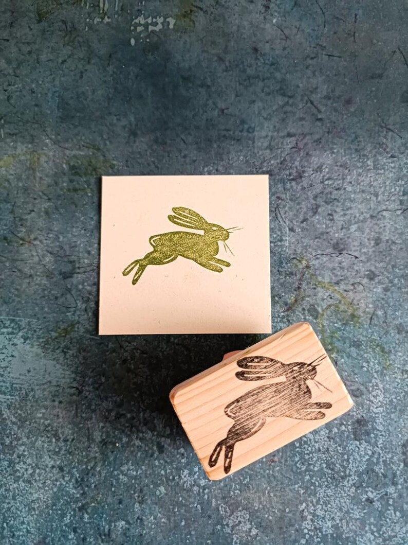 May include: A wooden stamp with a black silhouette of a rabbit jumping. The stamp is on a white card with a green silhouette of a rabbit jumping.