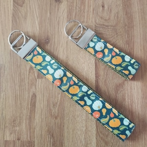 May include: Two keychains with silver key rings and green fabric straps with a pattern of orange, white, and yellow gourds.