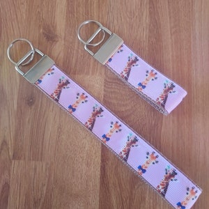 May include: Two pink and brown keychains with a giraffe pattern and a blue bow tie. The keychains have silver key rings.