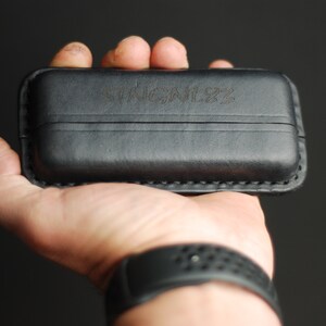 Puede incluir: Una funda de cuero negra con la palabra "STICKLER" grabada en la parte delantera.