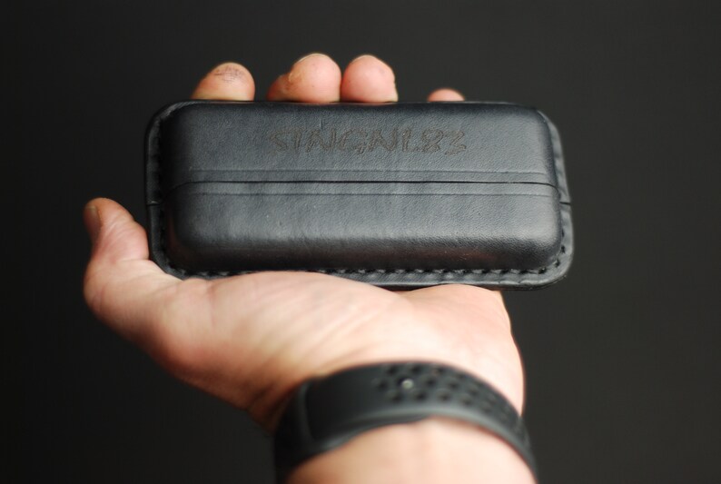 Puede incluir: Una funda de cuero negra con la palabra "STICKLER" grabada en la parte delantera.