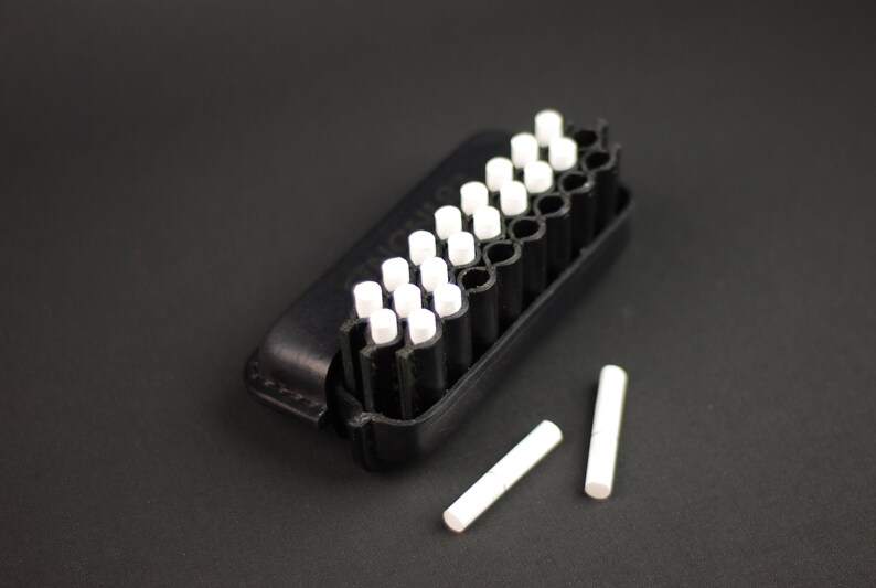 Puede incluir: Una caja negra con una fila de tizas blancas. Dos tizas adicionales est&aacute;n sobre una superficie negra.