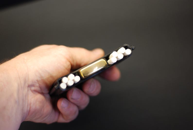 May include: A black rectangular case featuring a central gold-toned metal lighter flanked by two rows of white cylindrical sticks. The case is designed to hold the lighter securely in the middle while providing storage for the white sticks on both sides.