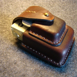 Puede incluir: Estuche de cigarrillos de cuero marrón hecho a mano, con tapa con bisagras y cierre de botón de latón. La funda está cosida con hilo blanco y contiene un paquete de cigarrillos.