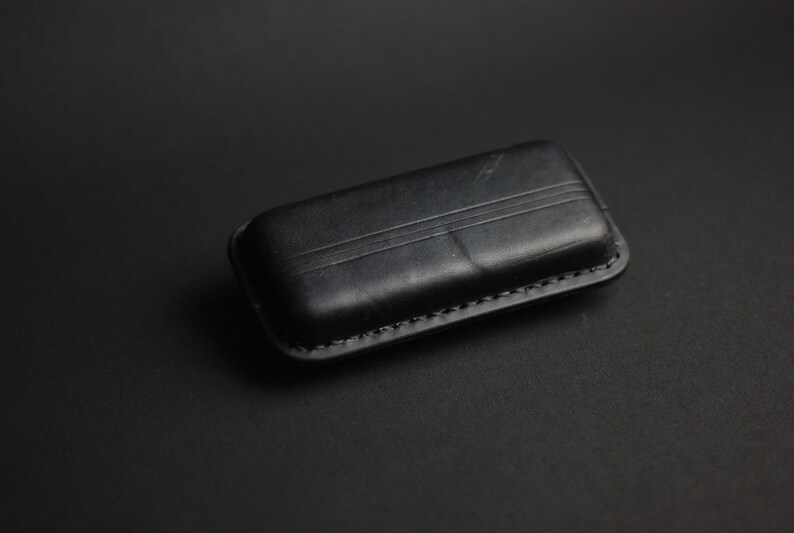 Puede incluir: Una funda de cuero negra con un borde cosido.