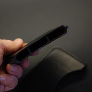 May include: A black leather card holder featuring two distinct interior compartments for storage. The item has visible stitching along the edges and a slim, rectangular profile designed to hold multiple cards securely in a compact, organized manner.