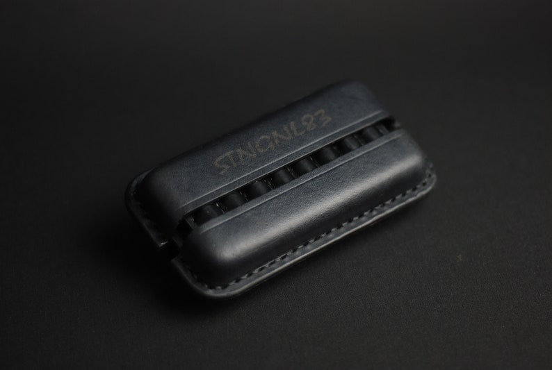 Puede incluir: Una funda de cuero negro con el texto "STENCIL92" grabado en la parte superior. La funda tiene m&uacute;ltiples ranuras para guardar objetos peque&ntilde;os.