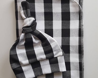 May include: Black and white checked baby blanket and matching knotted hat. The blanket is folded in half and the hat is placed on top of it.