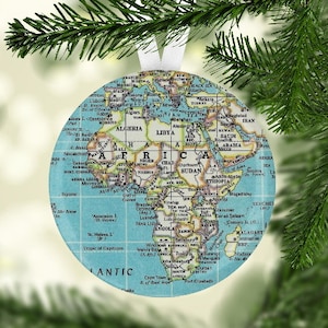 May include: A round, blue and white Christmas ornament featuring a vintage world map with the continent of Africa highlighted. The ornament includes the text "ATLANTIC" at the bottom.