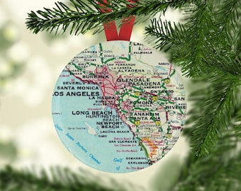 May include: A round, blue and white Christmas ornament featuring a map of Southern California. The map shows major cities and highways. The ornament is decorated with a red ribbon.
