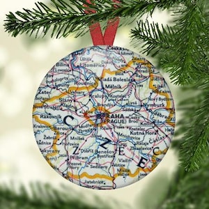 May include: A round, colorful ornament featuring a map of the Czech Republic with the city names labeled. The ornament is decorated with a red ribbon and the word "CZECH" is written in large letters.