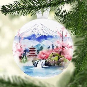 May include: A white Christmas ornament with a watercolor painting of Mount Fuji, a red pagoda, cherry blossoms, and a waterfall.
