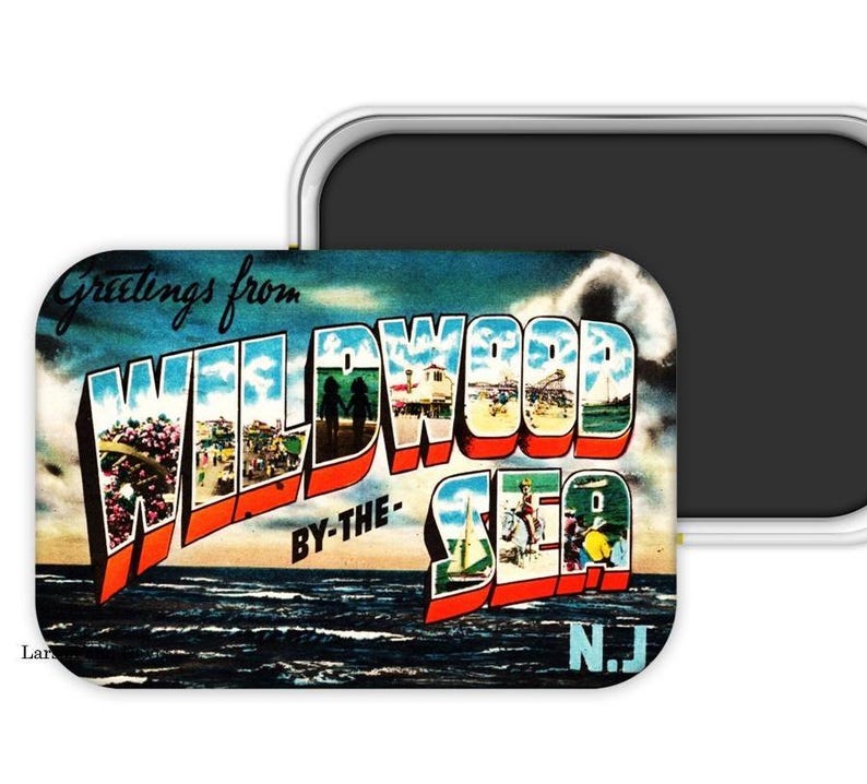 May include: A rectangular magnet featuring a vintage postcard design. The magnet displays the words "Greetings from WILDWOOD BY-THE-SEA N.J." in bold, colorful letters. The background shows a beach scene with ocean waves and a blue sky.
