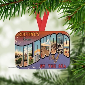 May include: Rectangular Christmas ornament with a vintage postcard design. The ornament reads "GREETINGS from WILDWOOD NJ BY THE SEA" in a stylized font, with images of a beach and boardwalk. It has a red ribbon for hanging.