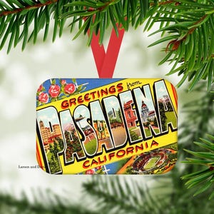 May include: A rectangular Christmas ornament featuring a vintage postcard design with the words "Greetings from Pasadena California." The ornament has a red ribbon for hanging and is surrounded by green pine needles.