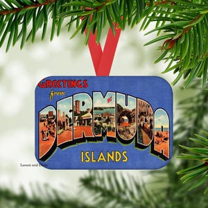 May include: A rectangular Christmas ornament with a blue background features the words "Greetings from Bermuda Islands" in a vintage postcard style. The ornament is suspended by a red ribbon and framed by green pine needles.