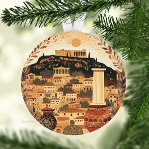 May include: Round Christmas ornament featuring a detailed illustration of a cityscape with a mountain, buildings, and a sun. The ornament has a white ribbon for hanging and is decorated with a green and brown color scheme.