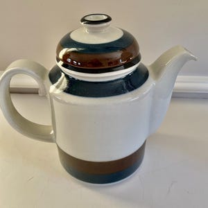 May include: A white ceramic coffee pot with a brown and blue striped design. The pot has a lid with a matching design.