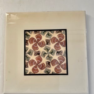 May include: A white ceramic tile with a black frame surrounding a colorful image of a repeating pattern of brown, green, and white geometric shapes.