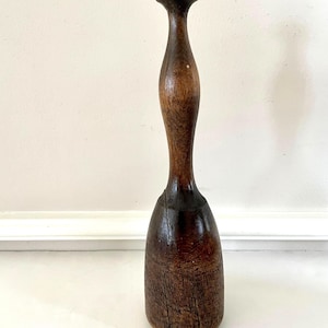 May include: A vintage wooden muddler with a rounded top and a bulbous base. The dark brown wood shows visible grain and signs of age, with a smooth, polished handle. The muddler is designed for mixing cocktails.