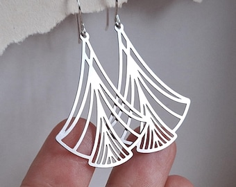 May include: A pair of silver earrings with an Art Deco design. The earrings have a fan-like shape with cut-out patterns. They are suspended from a simple hook.