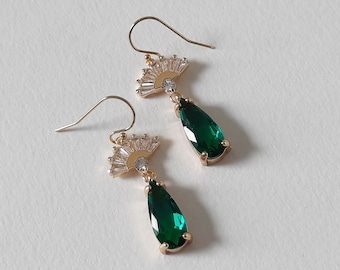 May include: Gold earrings with a teardrop-shaped green gemstone and a fan-shaped design of clear rhinestones.
