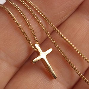 Puede incluir: Un collar dorado con un peque&ntilde;o colgante de cruz. La cruz tiene un dise&ntilde;o sencillo y cl&aacute;sico, suspendido de una delicada cadena. El collar se muestra sobre un fondo neutro, resaltando los detalles de la joya.