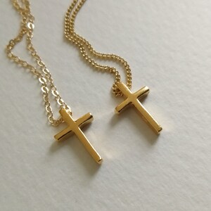 Puede incluir: Dos collares con cruces doradas. Cada collar presenta una cadena delicada y un colgante de cruz simple y pulido. Las cruces est&aacute;n centradas y tienen una superficie lisa y reflectante. El fondo es de color blanco roto.