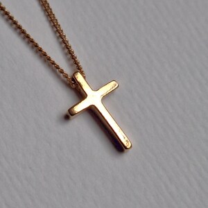 Puede incluir: Un collar con colgante de cruz de color dorado. La cruz tiene un dise&ntilde;o simple y cl&aacute;sico con bordes redondeados. La cadena es delicada y tambi&eacute;n dorada. El collar se muestra sobre un fondo suave y neutro.