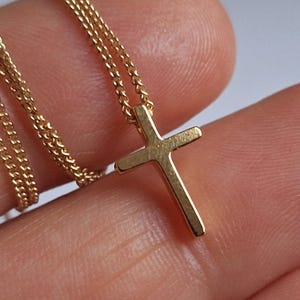 Puede incluir: Un collar con colgante de cruz dorada. La cruz es de dise&ntilde;o sencillo, suspendida de una delicada cadena. El collar se muestra sobre un fondo neutro, resaltando los detalles de la joya.