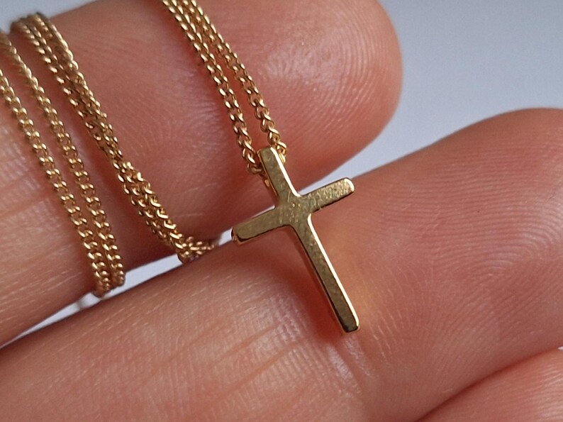 Puede incluir: Un collar con colgante de cruz dorada. La cruz es de dise&ntilde;o sencillo, suspendida de una delicada cadena. El collar se muestra sobre un fondo neutro, resaltando los detalles de la joya.