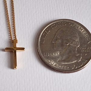 Puede incluir: Un collar con colgante de cruz de color dorado y una cadena delicada. La cruz es peque&ntilde;a y de dise&ntilde;o sencillo. Una moneda de veinticinco centavos estadounidense est&aacute; junto al collar para comparar el tama&ntilde;o.