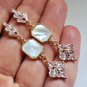 Puede incluir: Pendientes de oro con una piedra octogonal de nácar blanco y un racimo de cristales transparentes.