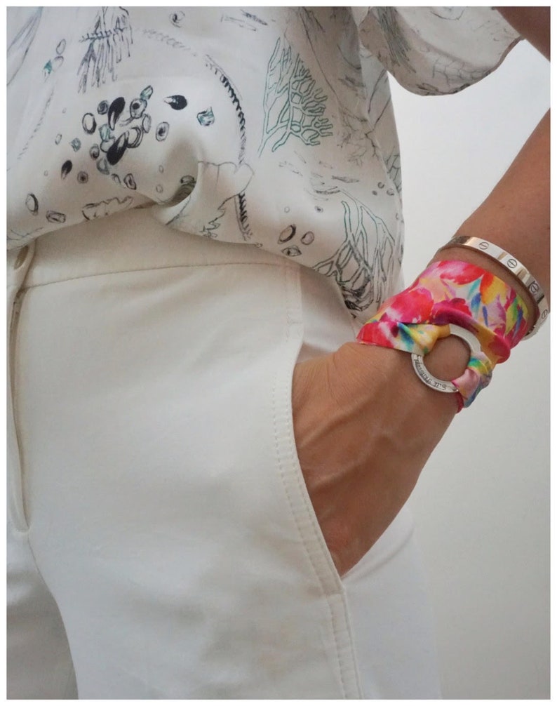 May include: White pants with a pocket and a colorful patterned scarf tied around the wrist with a silver ring.
