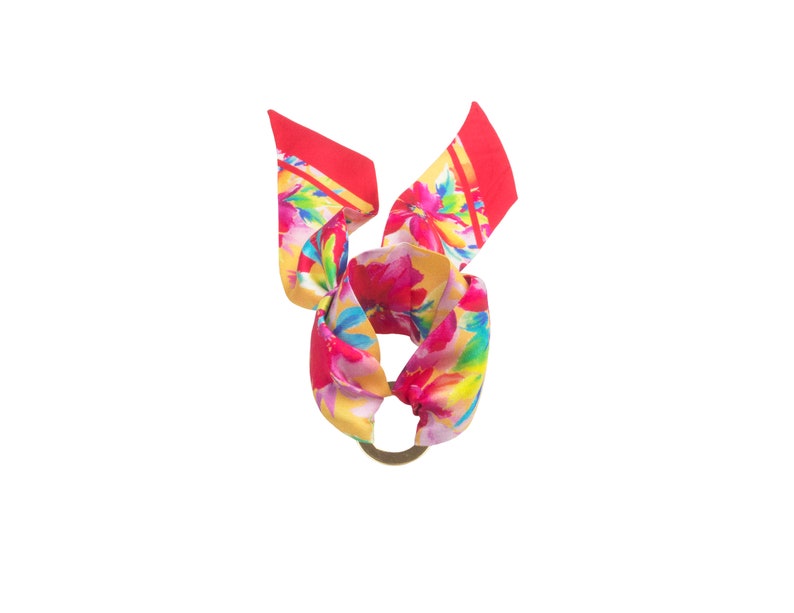 May include: A red, yellow, and pink floral patterned silk scarf tied in a knot with a gold ring.