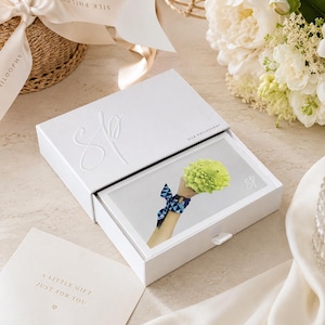 May include: A white rectangular sliding gift box with the embossed letters SP and the text SILK PHILOSOPHY. Inside, a card displays a graphic of a wrist wearing a blue patterned silk ribbon and holding a bright green romanesco broccoli.