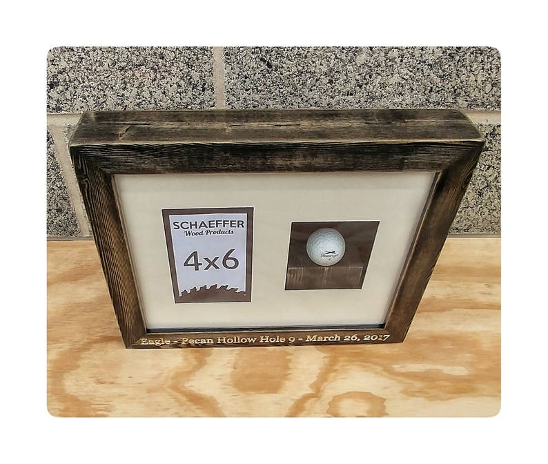 Puede incluir: Un marco de madera oscura con un acabado envejecido que contiene una pelota de golf y un espacio de 4x6 pulgadas para una foto. El texto en el marco dice "Eagle - Pecan Hollow Hole 9 - March 26, 2017."