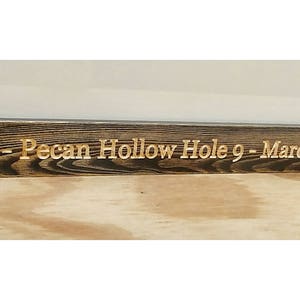 Puede incluir: Un marco de fotos de madera te&ntilde;ida oscura con las palabras "Eagle - Pecan Hollow Hole 9 - March 26, 2017" grabadas en letras doradas. El marco tiene un dise&ntilde;o simple y r&uacute;stico.
