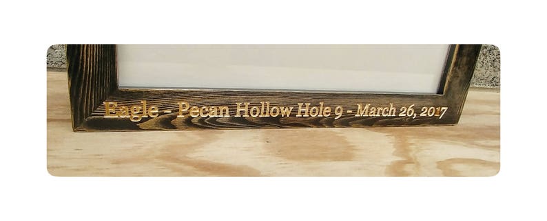 Puede incluir: Un marco de fotos de madera te&ntilde;ida oscura con las palabras "Eagle - Pecan Hollow Hole 9 - March 26, 2017" grabadas en letras doradas. El marco tiene un dise&ntilde;o simple y r&uacute;stico.