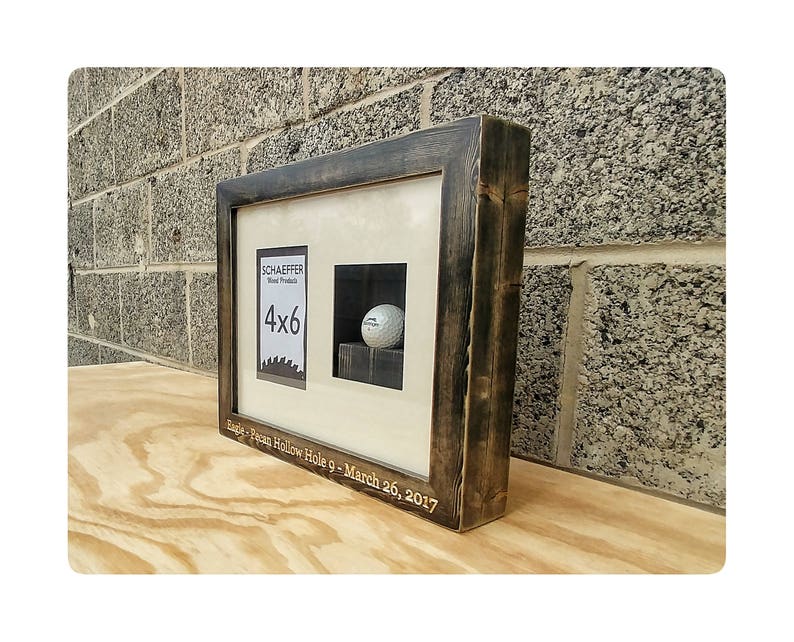 Puede incluir: Una exhibici&oacute;n enmarcada con un marco de madera te&ntilde;ida oscura. La exhibici&oacute;n presenta una abertura para fotos de 4x6 y un &aacute;rea empotrada que contiene una pelota de golf. El texto "SCHAEFFER Wood Products" y "Eagle - Pecan Hollow Hole 9 - March 26, 2017" son visibles.
